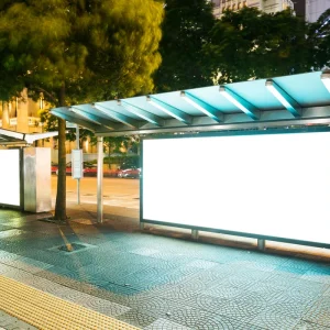 Parada de autobús iluminada con grandes espacios publicitarios en una avenida nocturna.