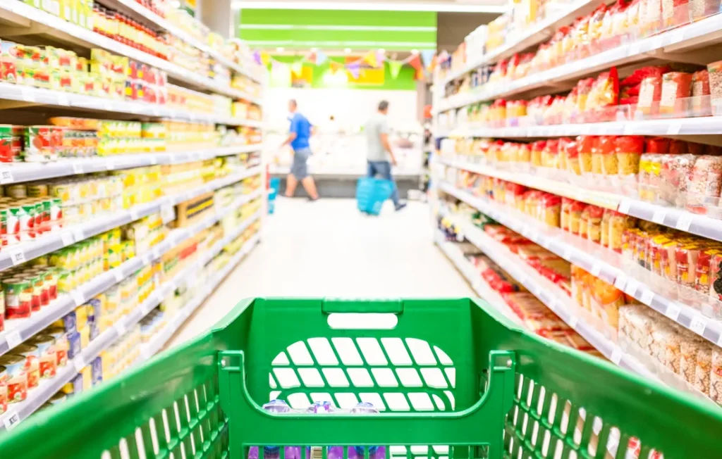 Carrito verde avanza entre pasillos con productos dentro de un supermercado.