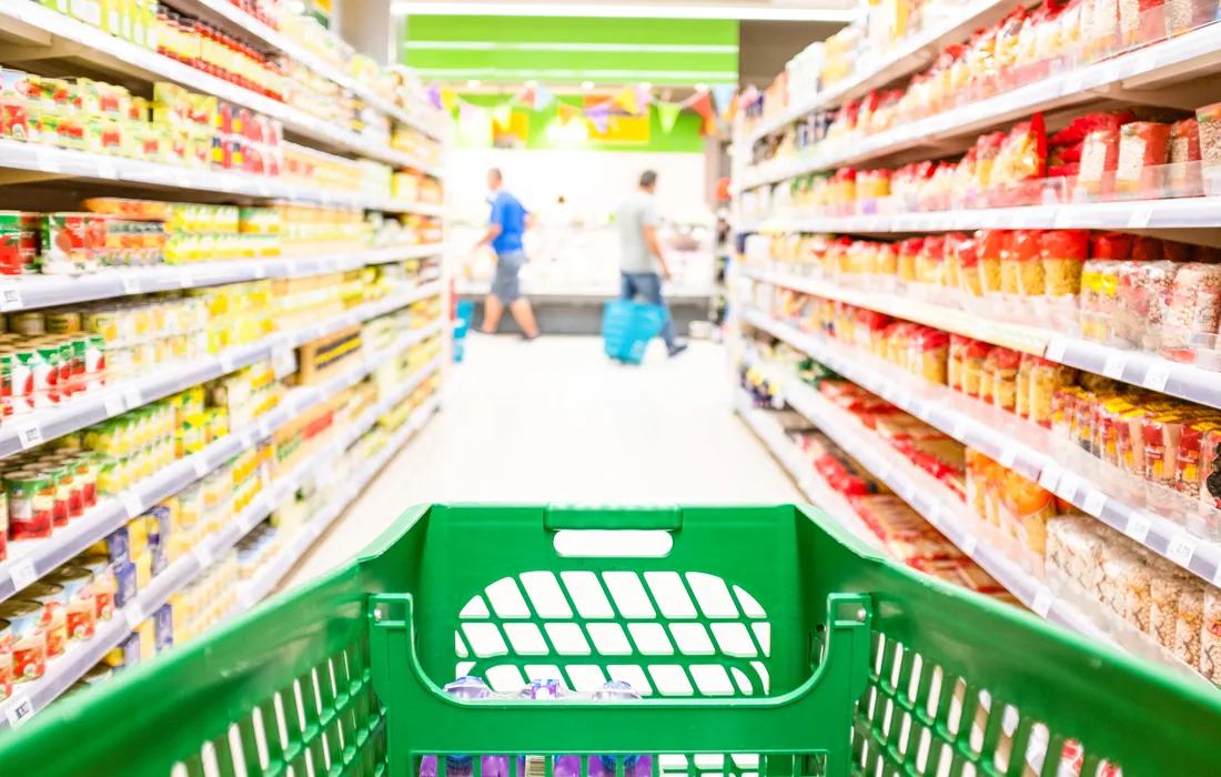 Carrito verde avanza entre pasillos con productos dentro de un supermercado.