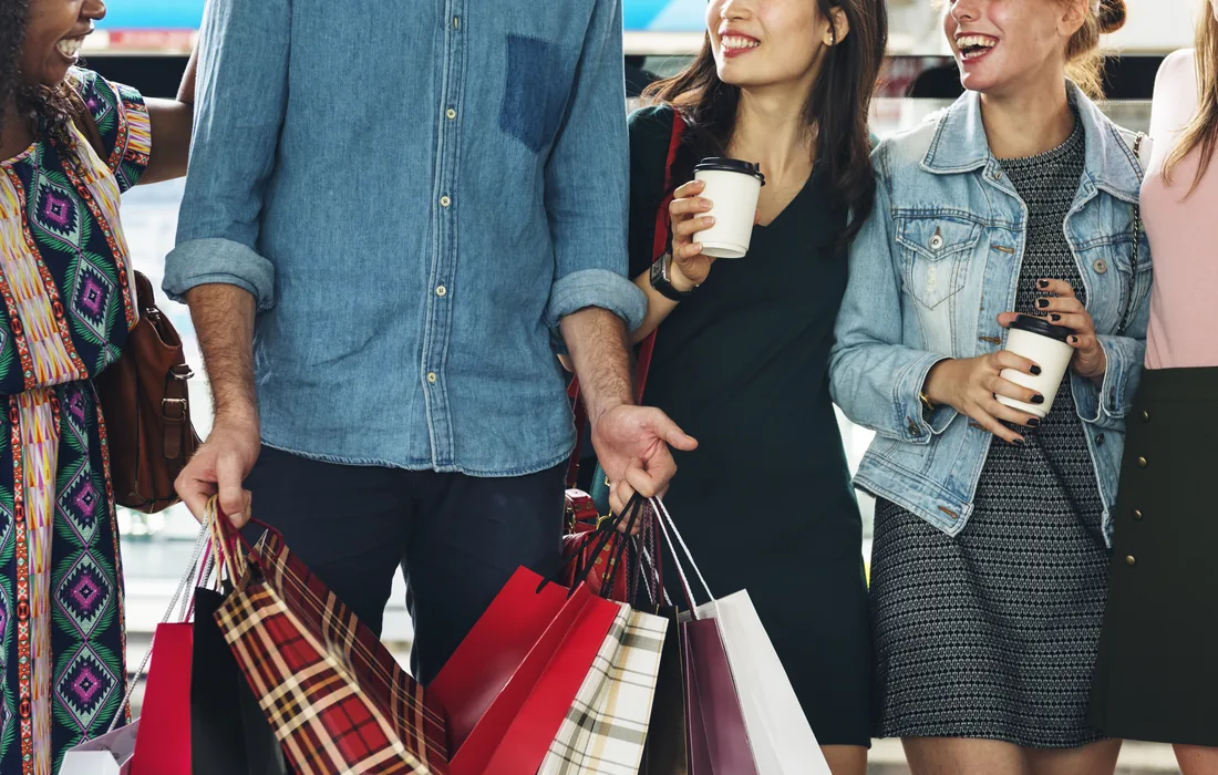 Grupo de amigos sonríe mientras carga bolsas de compras y bebidas.